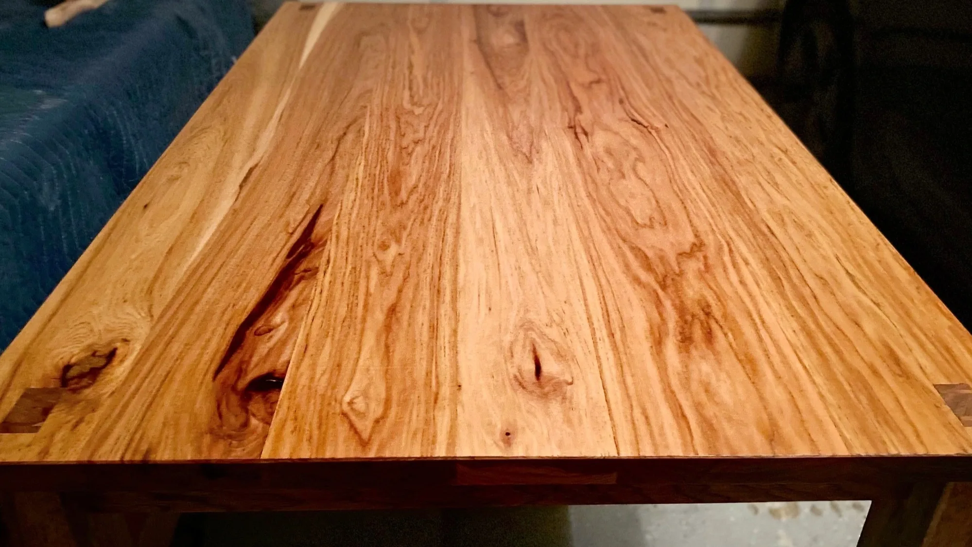 The top of a hickory table, boards running from pale to dark with knots left in and tenon ends showing at the corners.