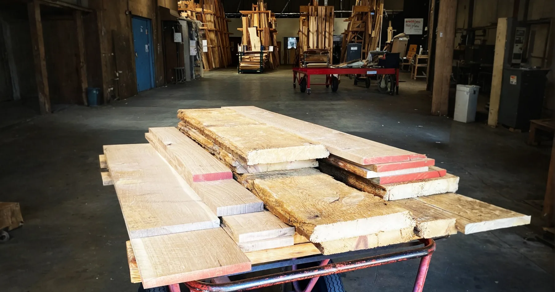 A cart stacked with S3S and rough boards, end-sealed in red, on the floor of a lumber yard with full racks behind.